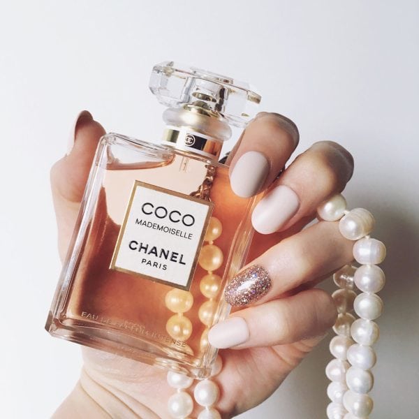 Hand holding a bottle of COCO MADEMOISELLE Eau de Parfum Intense by CHANEL with pearl bracelet and neutral manicure for an elegant luxury fragrance aesthetic.