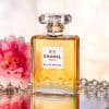 CHANEL N°5 Eau de Parfum perfume bottle surrounded by pink flowers and crystal gems with reflective luxury styling.