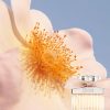 Chloé Eau de Parfum bottle placed in front of a large blooming flower with soft pastel floral background tones.