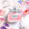 DIOR Miss Dior Eau de Parfum bottle styled with pink and purple flowers, fashion sketches, and soft couture-inspired floral artwork.