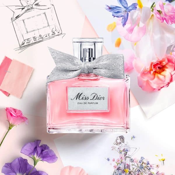 DIOR Miss Dior Eau de Parfum bottle styled with pink and purple flowers, fashion sketches, and soft couture-inspired floral artwork.